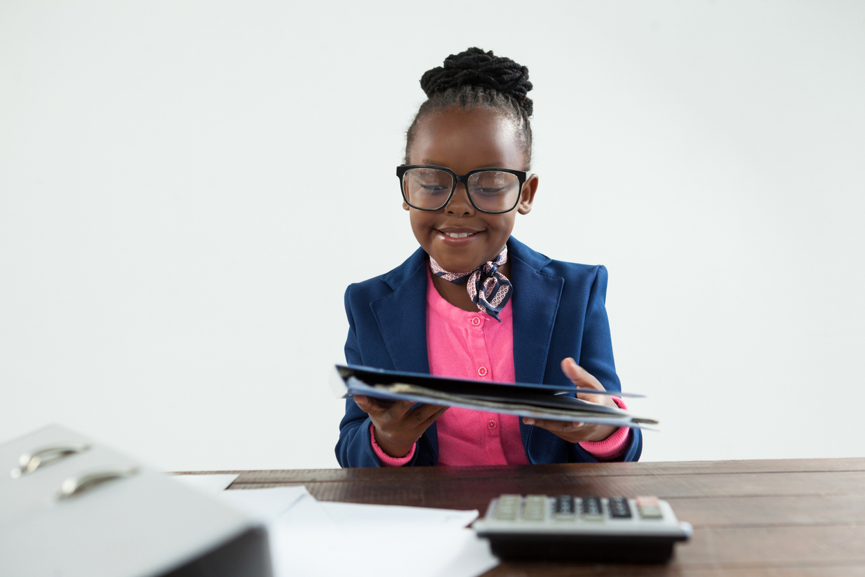 Young girl in a blazer and glasses reviewing a folder at a desk