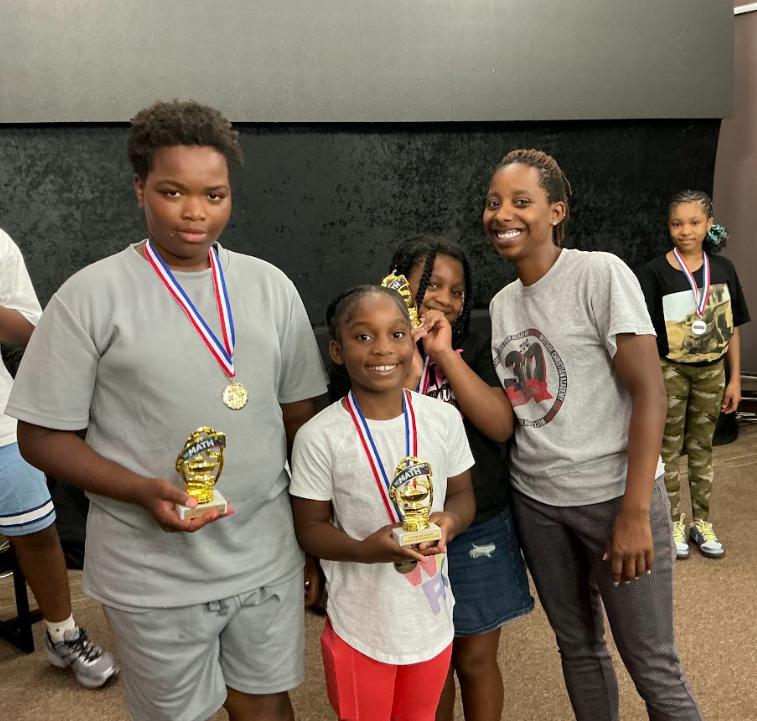 Camp Ignite students proudly holding math trophies with their mentor