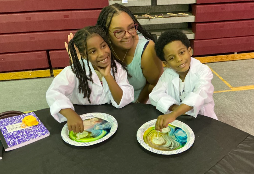 Three smiling campers in lab coats with colorful science experiments