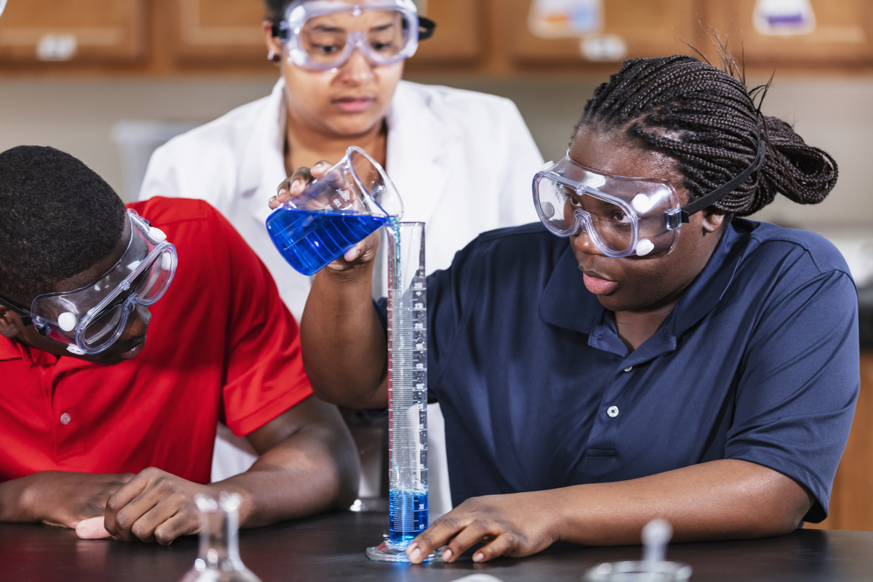 Students in goggles measuring blue liquid in a science lab