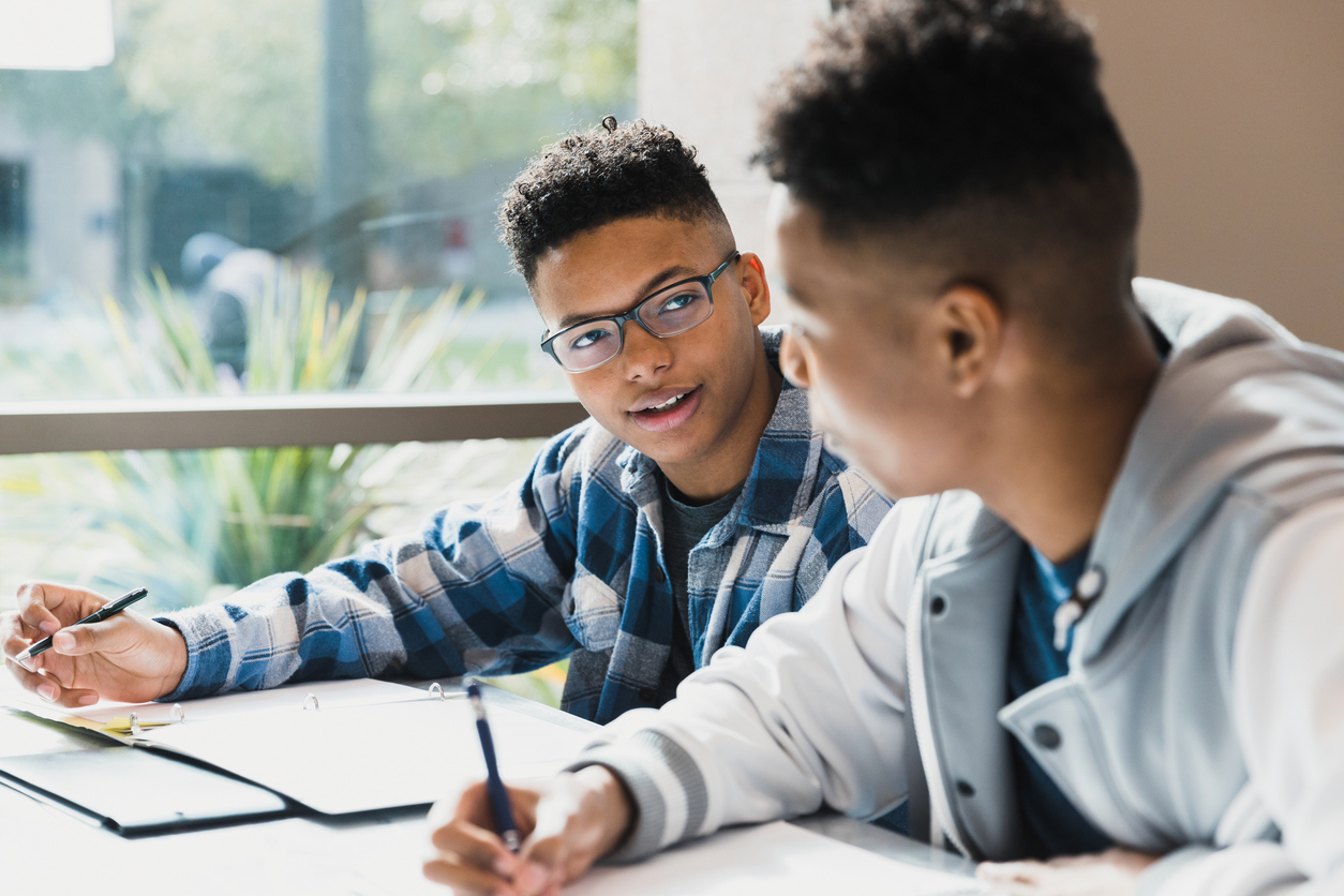 Two teen students studying and talking together at a desk