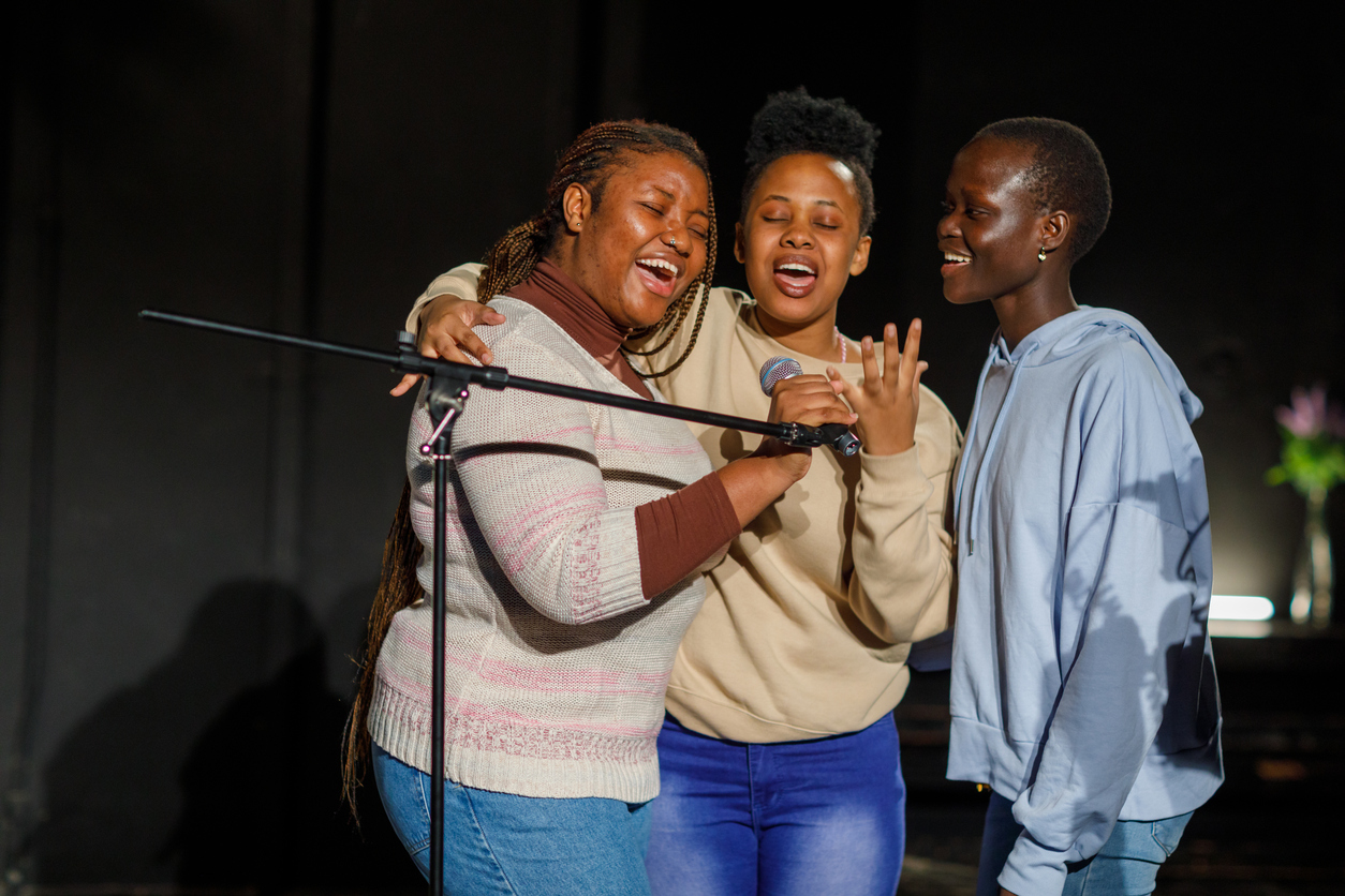 Three young vocalists singing together around a microphone on stage